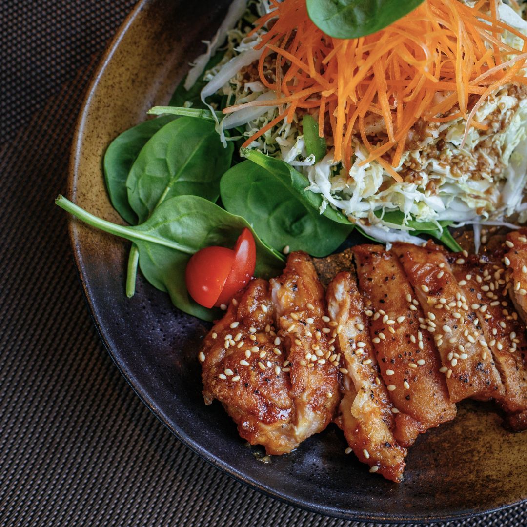 Plate of food with sesame chicken and spinach carrot tomato salad